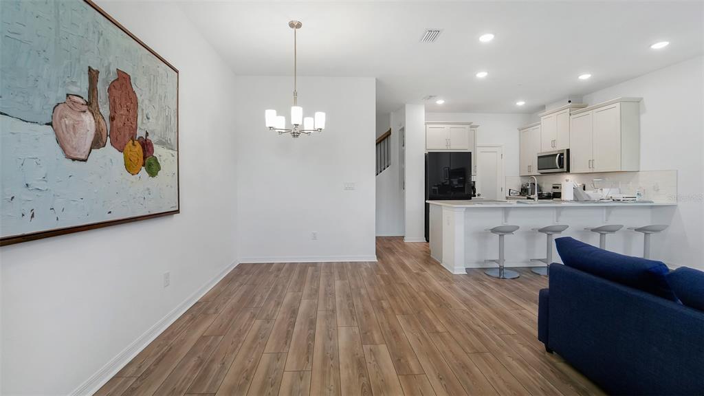 A dining area with a chandelier and large wall art opens to a modern kitchen — 11761 TIDAL ALLEY, ORLANDO, FL