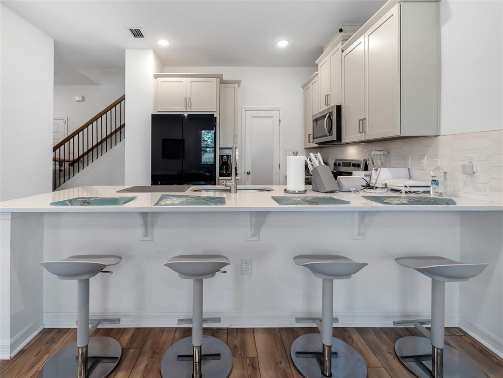 A kitchen features a white island with four bar stools, light cabinetry, and wood flooring — 11761 TIDAL ALLEY, ORLANDO, FL