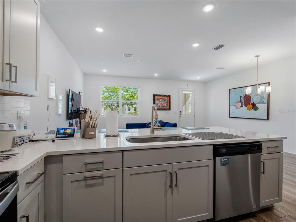 A kitchen island with a stainless steel sink and dishwasher faces a bright living area — 11761 TIDAL ALLEY, ORLANDO, FL