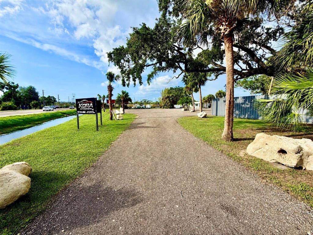 A gravel driveway leads toward a Kora Motorsports sign and trees on a sunny day — 1322 N PINELLAS AVENUE, TARPON SPRINGS, FL