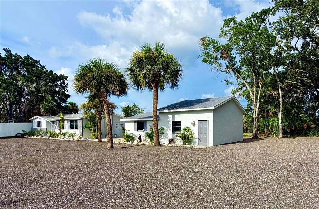A light-colored house with a detached garage sits on a large gravel lot with palms — 1322 N PINELLAS AVENUE, TARPON SPRINGS, FL