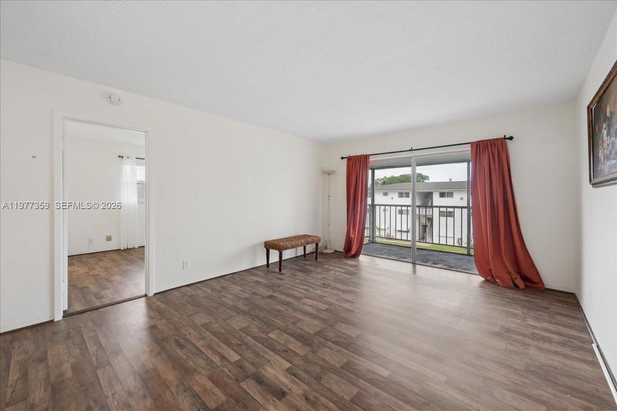 An empty living room features wood-look flooring, a sliding glass door, and a balcony view — 1200 Hillcrest Ct # 315, Hollywood FL 33021, HOLLYWOOD, FL
