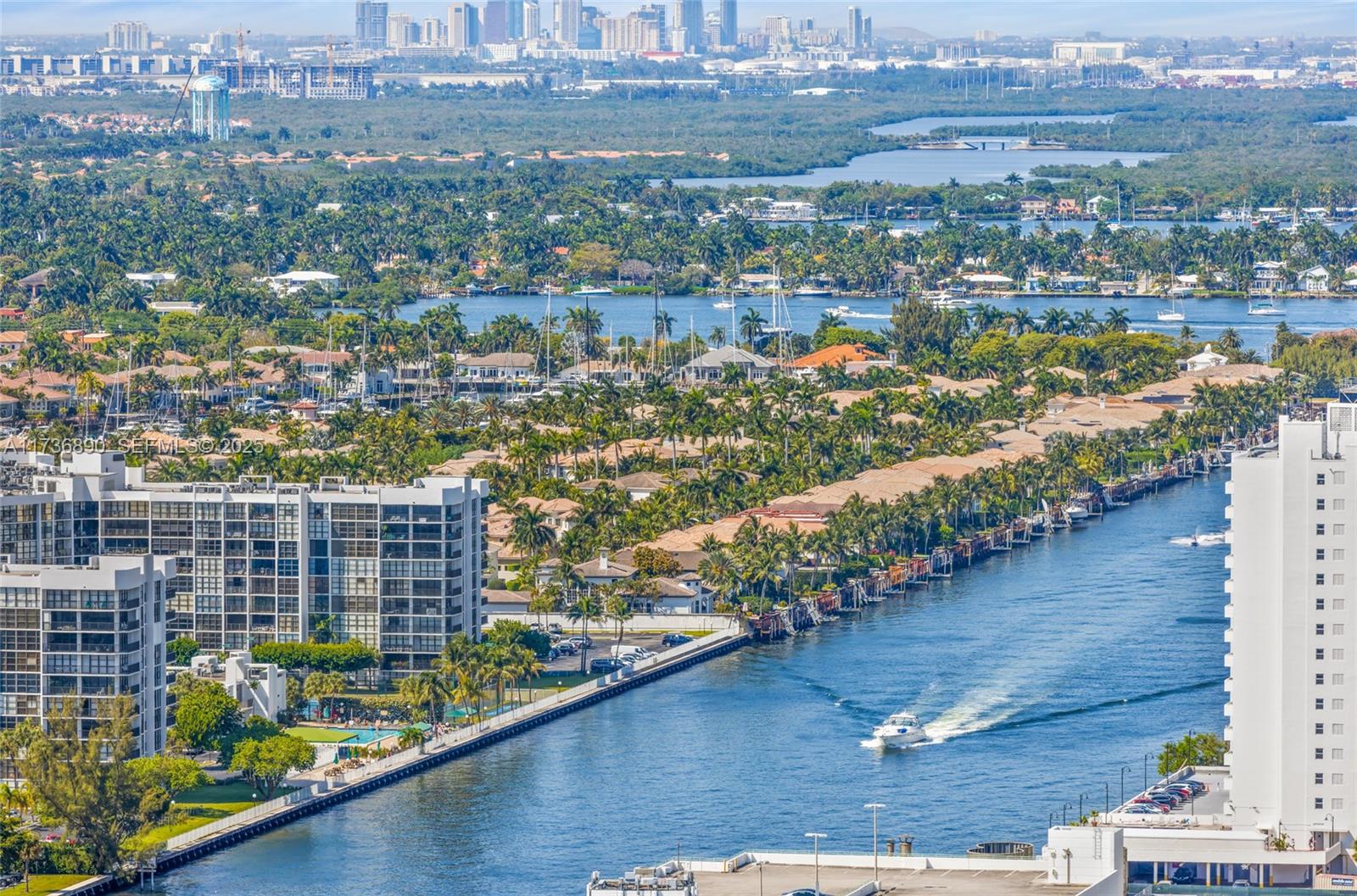 An aerial view shows a waterway with a boat passing between residential buildings and trees — 4111 S Ocean Dr # 2904, Hollywood FL 33019, HOLLYWOOD, FL
