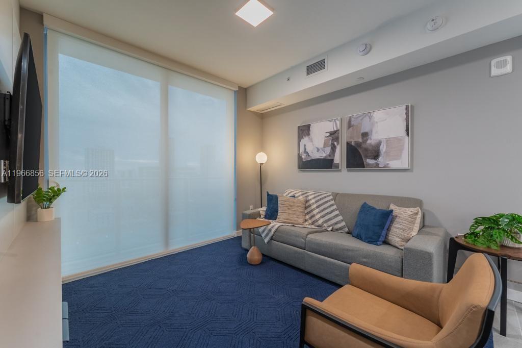 A living room features a grey sofa, a tan armchair, and blue patterned carpeting — 227 NE 2nd St # 1905, Miami FL 33132, MIAMI, FL