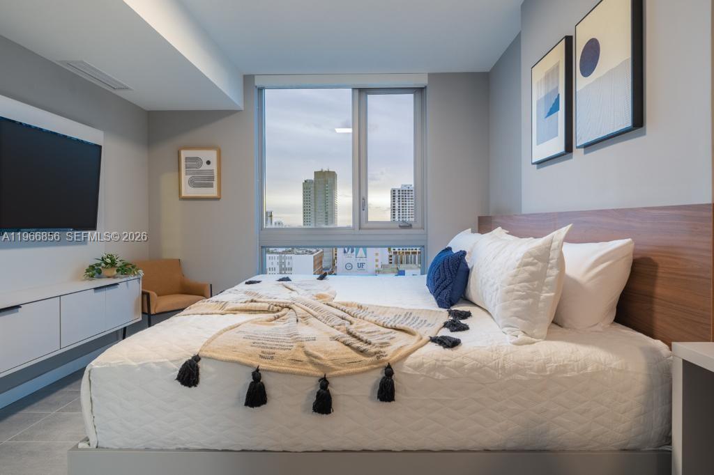 A modern bedroom features a bed with white bedding, a television, and a city view — 227 NE 2nd St # 1905, Miami FL 33132, MIAMI, FL