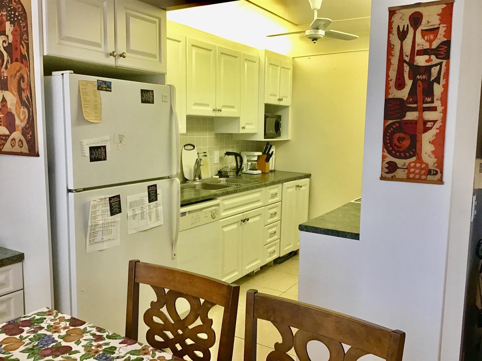 A kitchen with white cabinets, green countertops, and a white refrigerator next to a dining area — 4004 Exeter A, Boca Raton FL 33434, BOCA RATON, FL