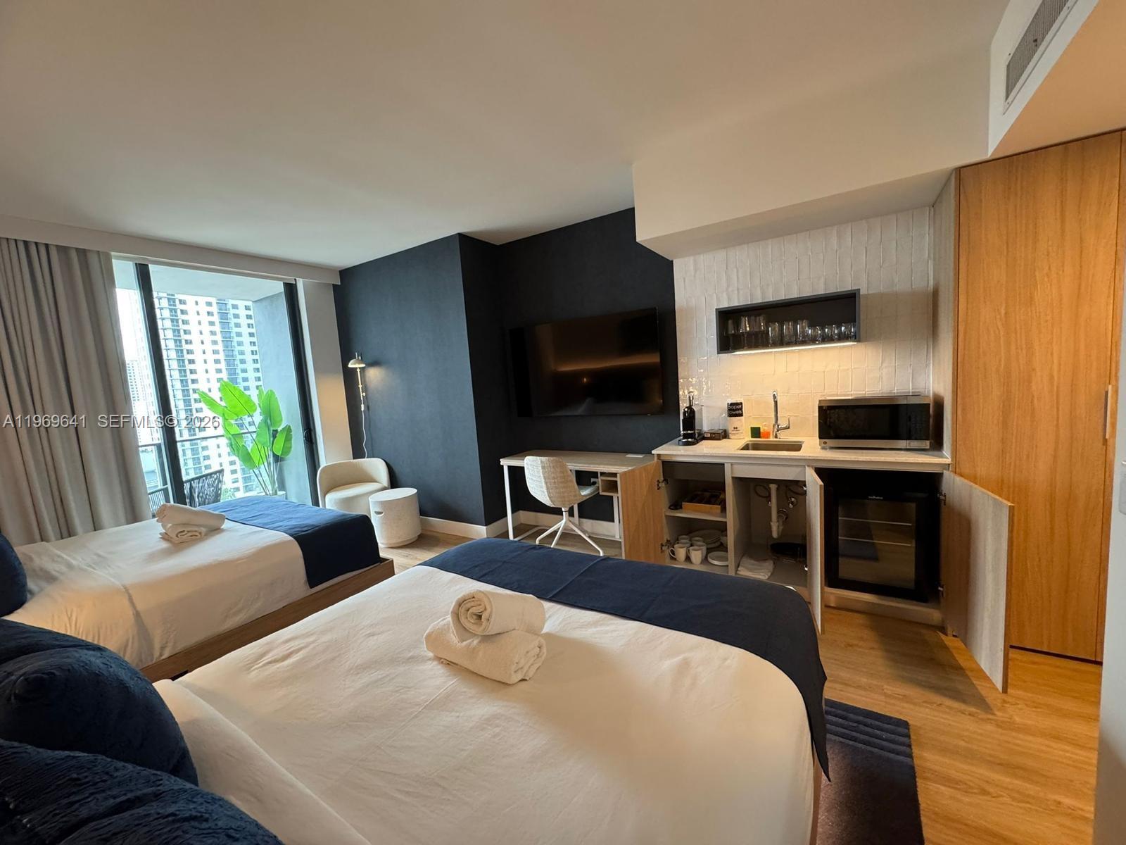 A hotel room features two beds, a kitchenette, a desk, and a view of buildings — 159 NE 6th St # 1806, Miami FL 33132, MIAMI, FL