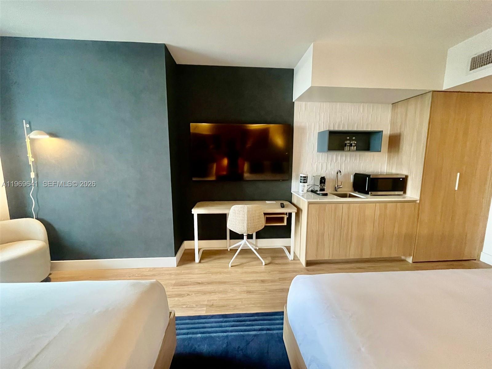 A hotel room features two beds, a desk, a kitchenette, and a dark accent wall — 159 NE 6th St # 1806, Miami FL 33132, MIAMI, FL