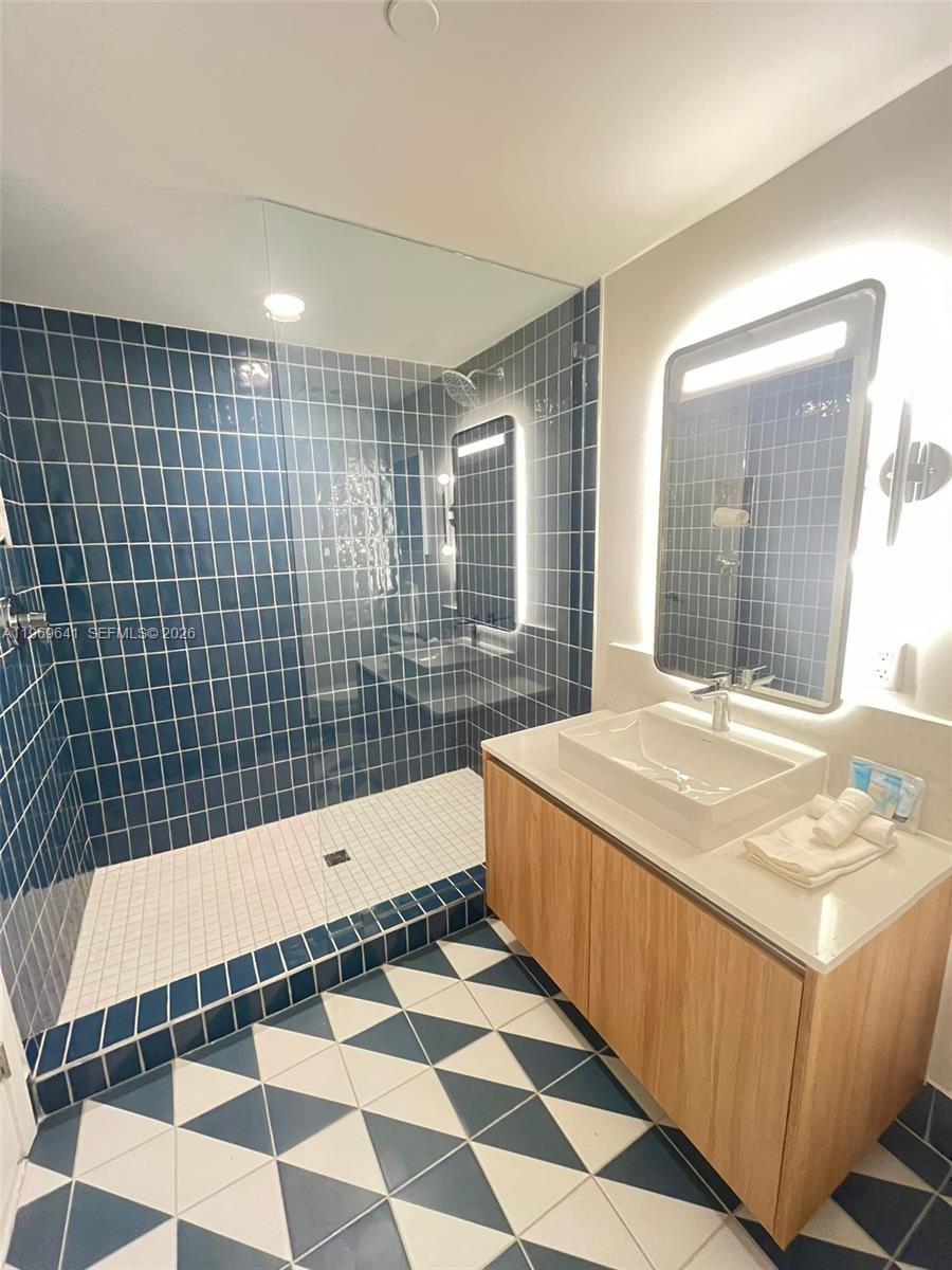 A bathroom features a blue-tiled walk-in shower, a wooden vanity, and geometric floor tiles — 159 NE 6th St # 1806, Miami FL 33132, MIAMI, FL