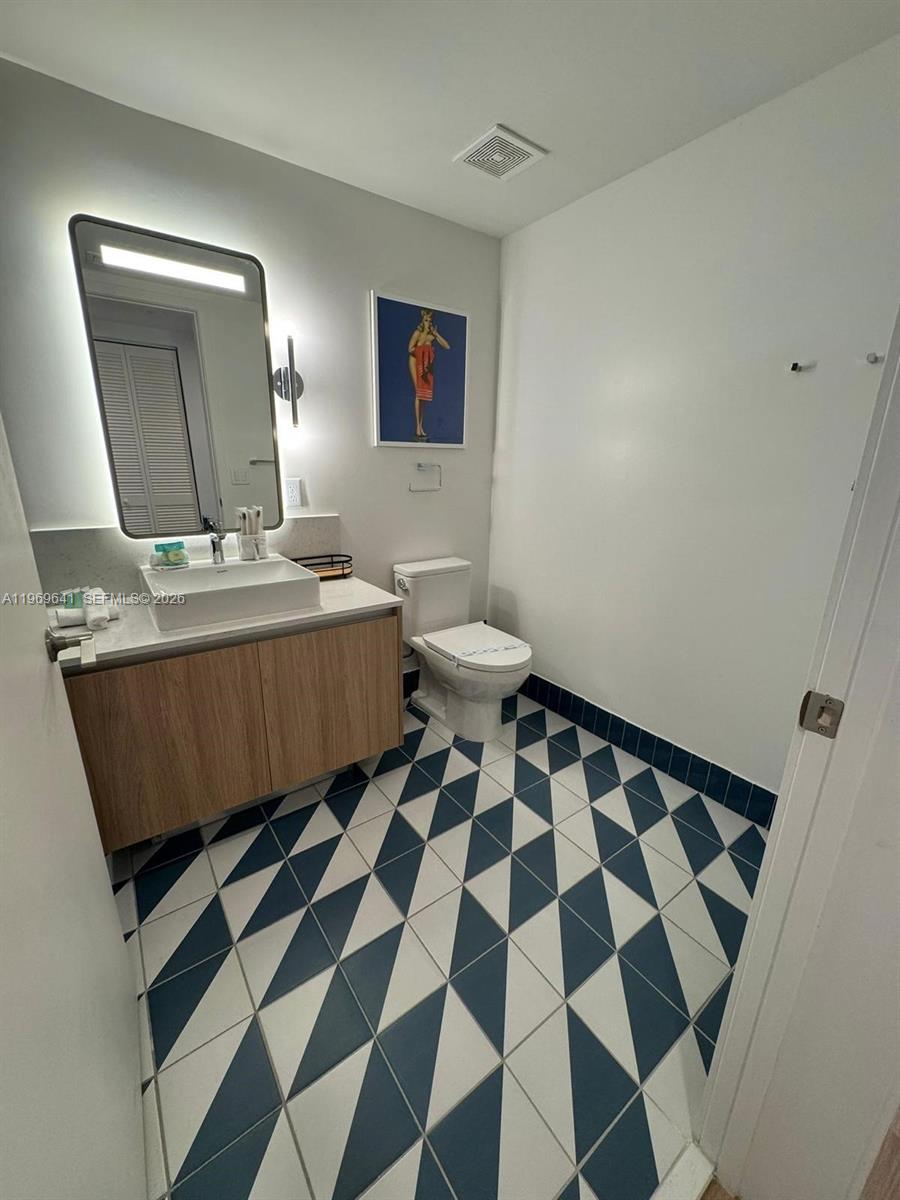 A bathroom features a floating vanity, a backlit mirror, and a geometric blue-and-white tiled floor — 159 NE 6th St # 1806, Miami FL 33132, MIAMI, FL