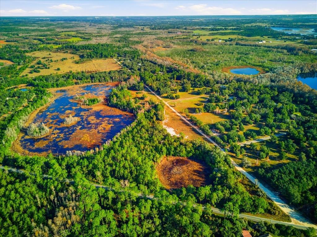 An aerial view shows a rural landscape with a large pond, wetlands, and wooded areas — LAKE ERIE RD, GROVELAND, FL