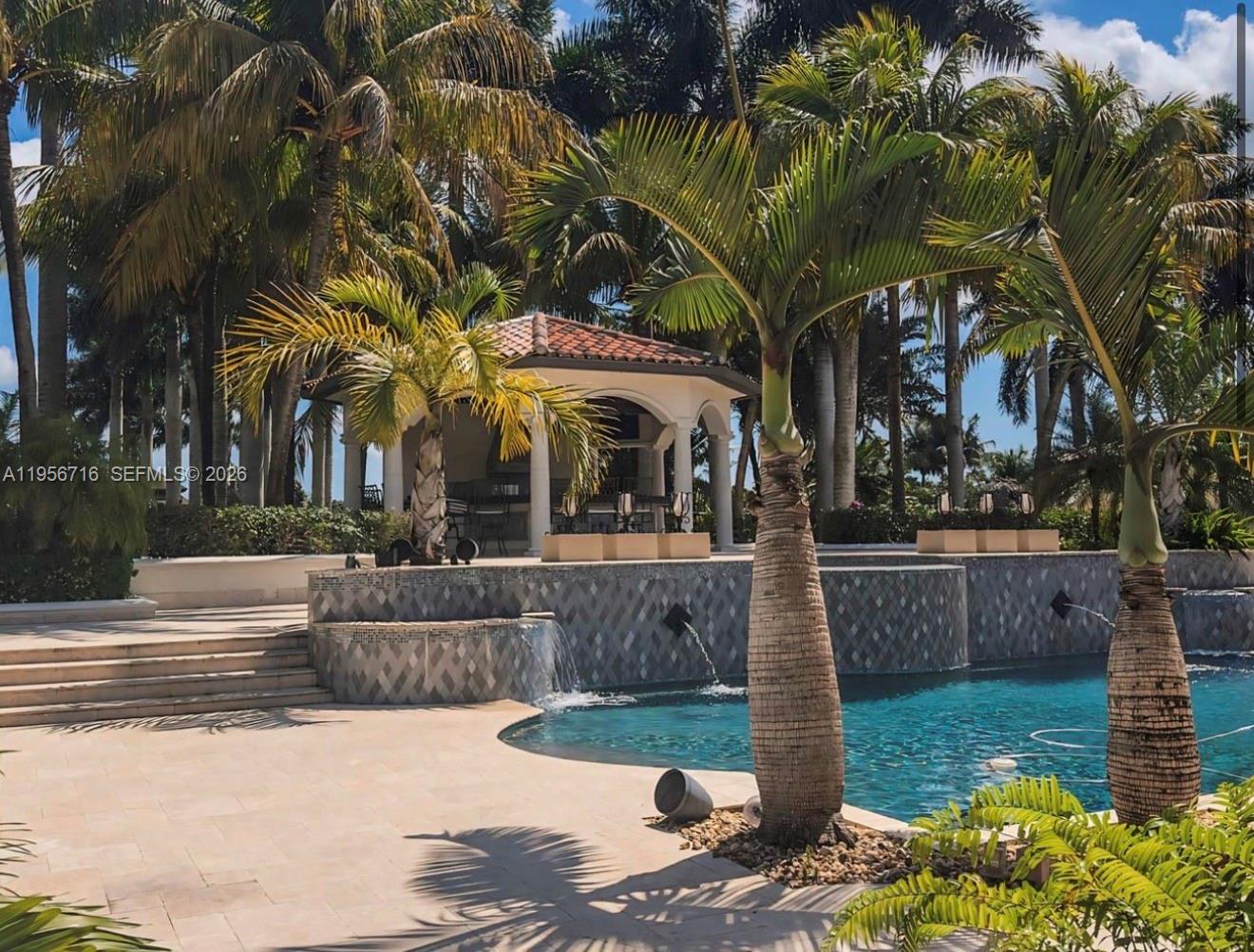 A swimming pool with water features sits in front of a covered patio and palms — 14949 SW 184th Ave, Miami FL 33196, MIAMI, FL