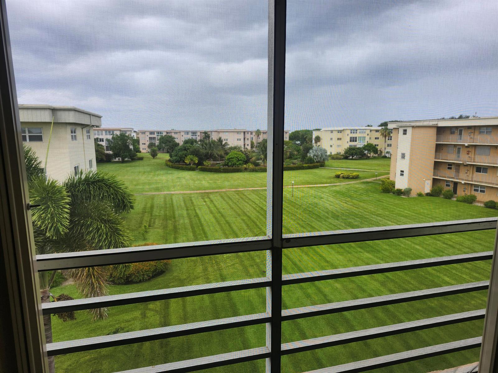 View from a balcony overlooking a large green lawn between several multi-story apartment buildings — 2600 NE 1st Lane # 402, Boynton Beach FL 33435, BOYNTON BEACH, FL
