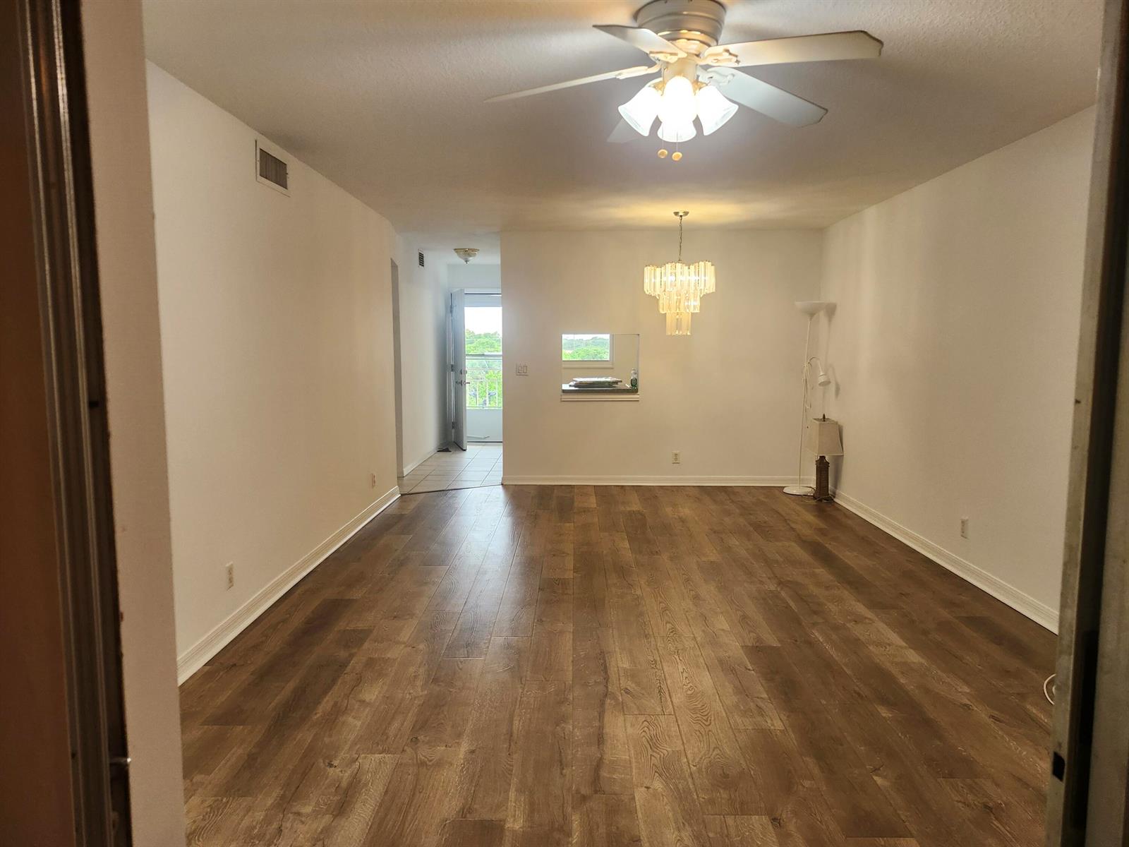 An empty living and dining area features wood-look flooring, a ceiling fan, and a chandelier — 2600 NE 1st Lane # 402, Boynton Beach FL 33435, BOYNTON BEACH, FL