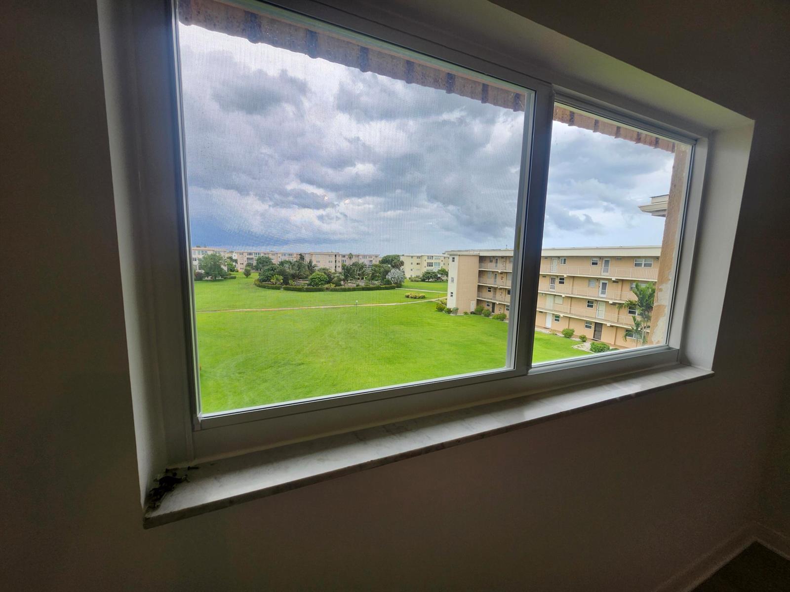 A view of a grassy courtyard and apartment buildings through a white-framed window — 2600 NE 1st Lane # 402, Boynton Beach FL 33435, BOYNTON BEACH, FL