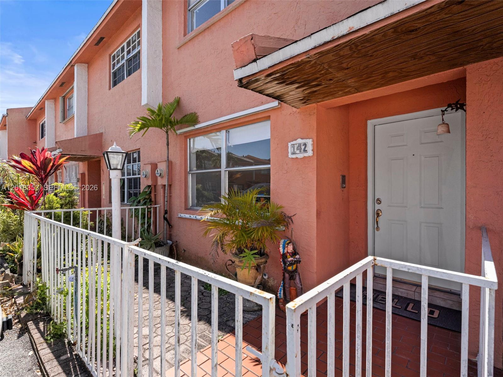 A peach-colored townhouse exterior features a white front door, a small porch, and metal railings — 100 SW 110th Ave # 142, Sweetwater FL 33174, SWEETWATER, FL