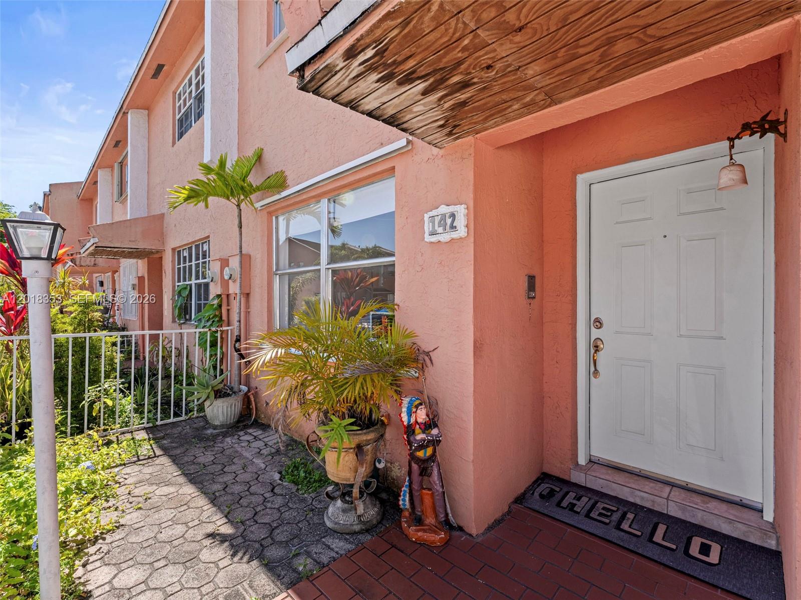 The exterior of a peach-colored townhouse features a white front door and a paved walkway — 100 SW 110th Ave # 142, Sweetwater FL 33174, SWEETWATER, FL