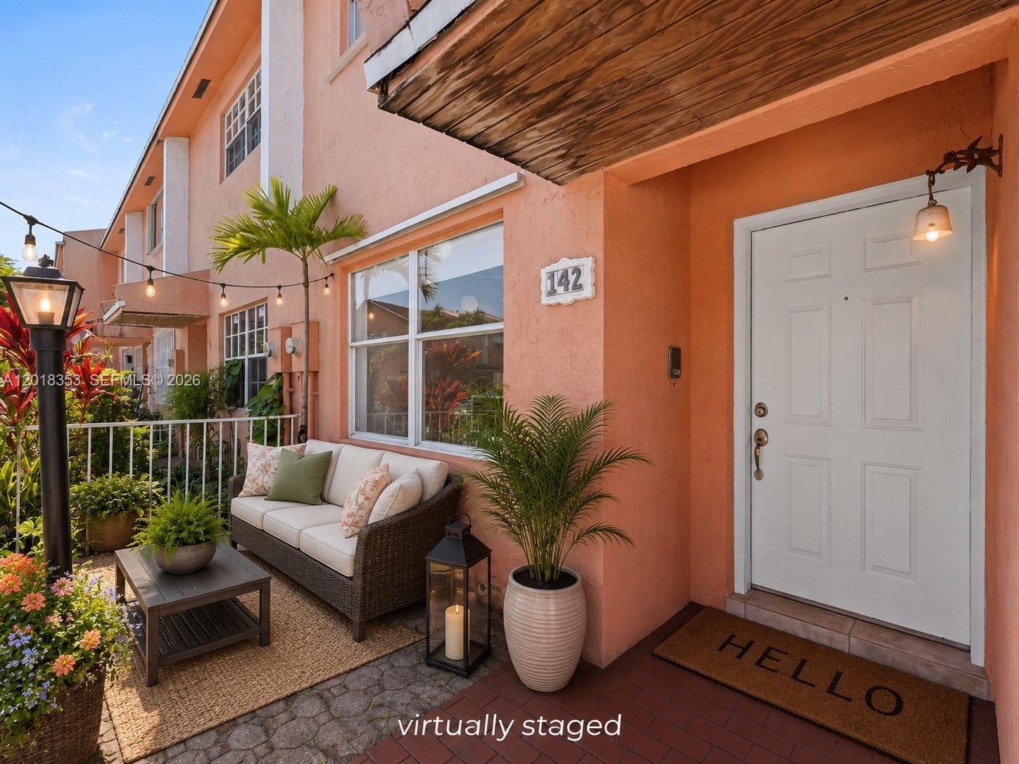 A peach-colored townhouse exterior features a patio with a sofa, coffee table, and front door — 100 SW 110th Ave # 142, Sweetwater FL 33174, SWEETWATER, FL