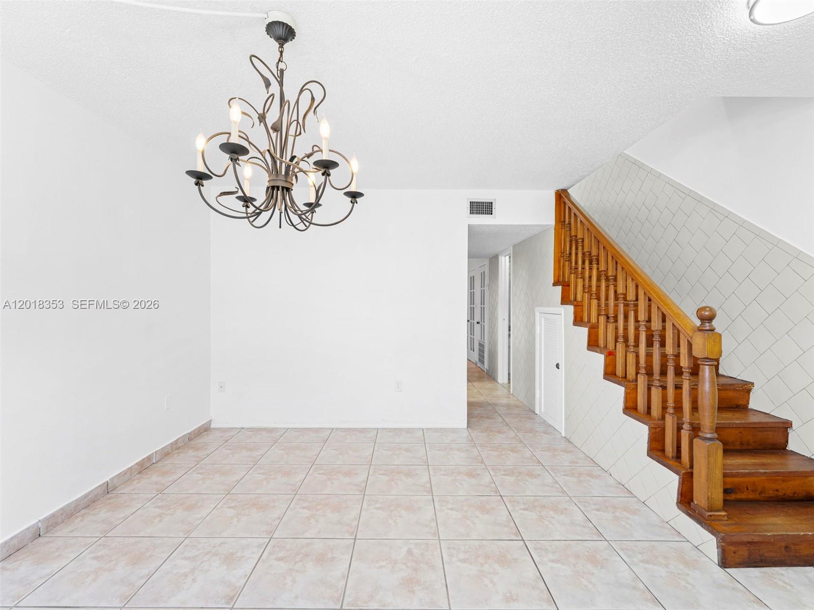 A dining area features a chandelier, tile flooring, and a wooden staircase with white tiling — 100 SW 110th Ave # 142, Sweetwater FL 33174, SWEETWATER, FL