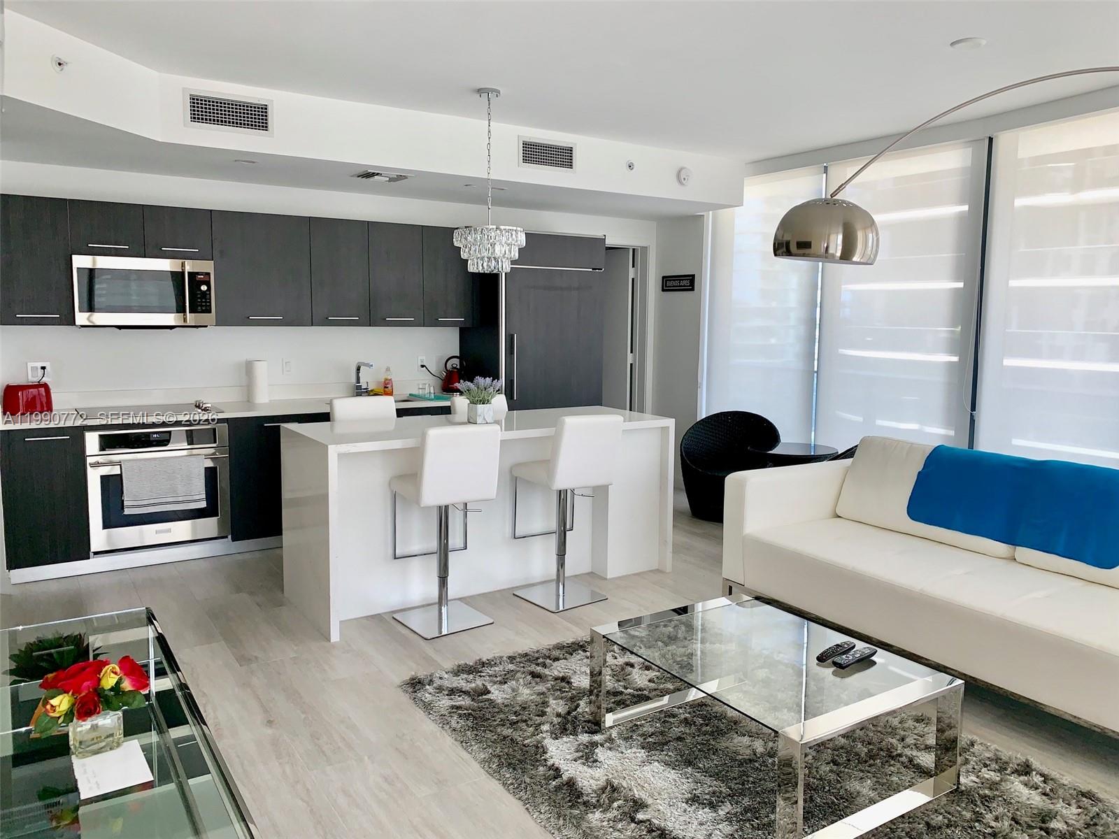 A modern open-concept kitchen and living area features dark cabinetry, white countertops, and a sofa — 55 SW 9 St # 2003, Miami FL 33130, MIAMI, FL