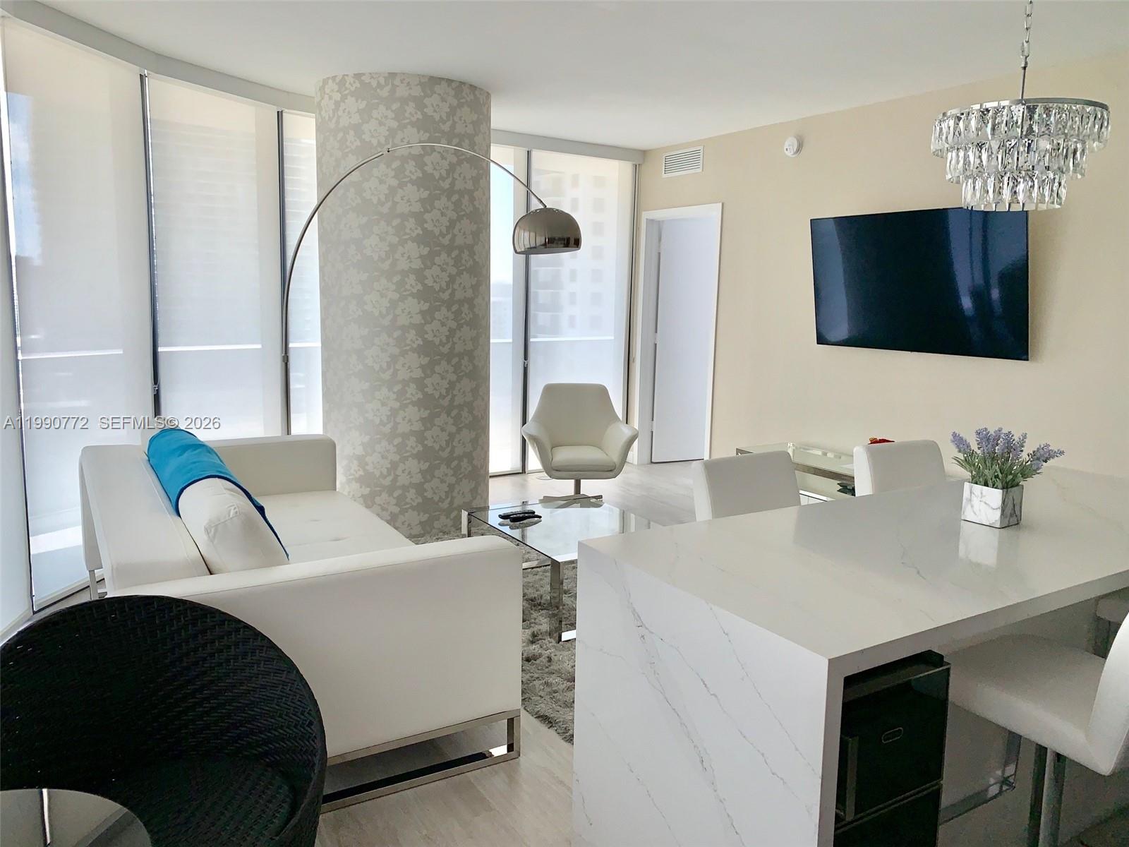 A modern living and dining area features white furniture, a marble-topped island, and floor-to-ceiling windows — 55 SW 9 St # 2003, Miami FL 33130, MIAMI, FL