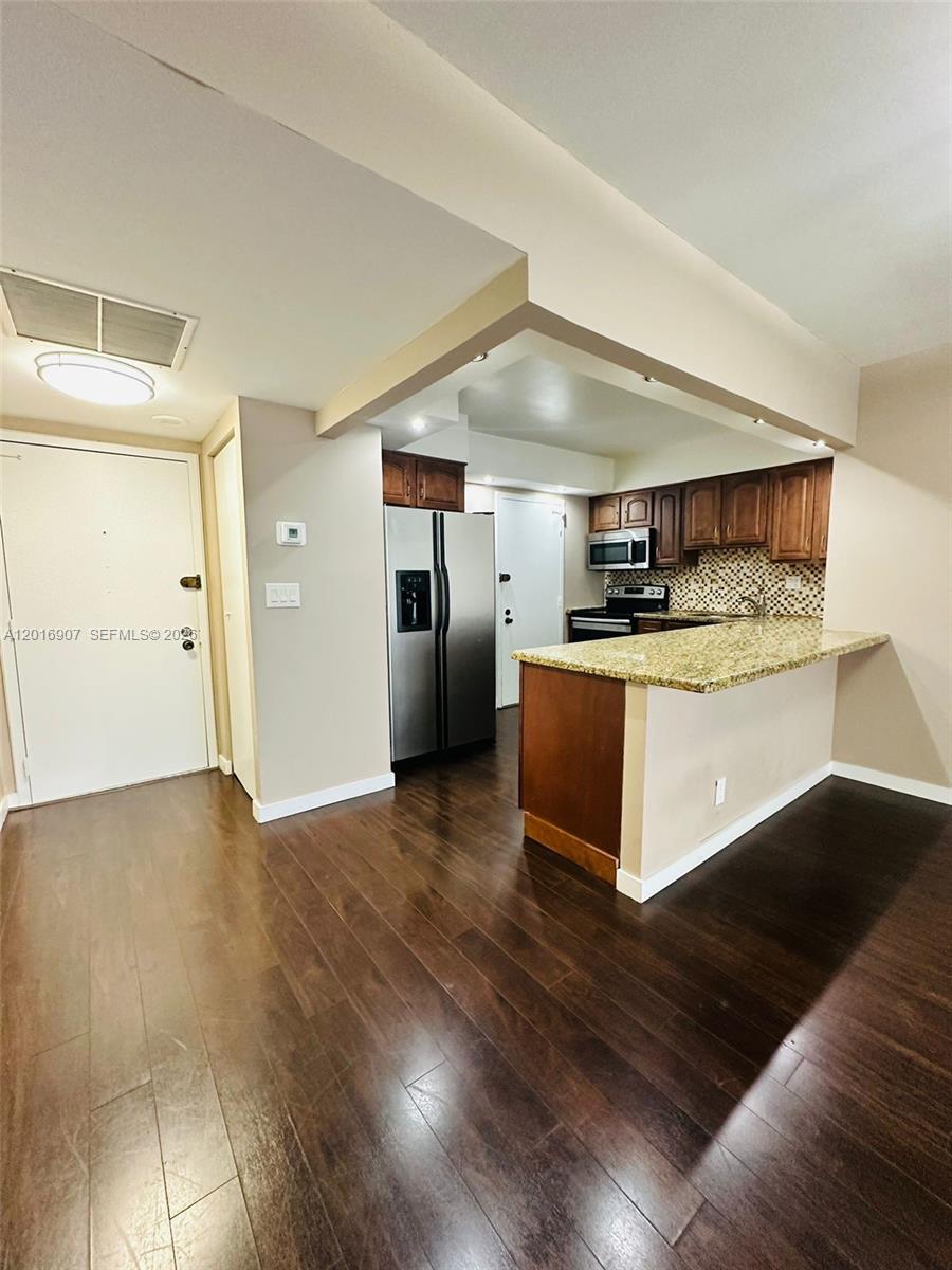 A kitchen with dark wood cabinets, granite countertops, and stainless steel appliances overlooks a room — 600 Three Islands Blvd # 304, Hallandale Beach FL 33009, HALLANDALE BEACH, FL