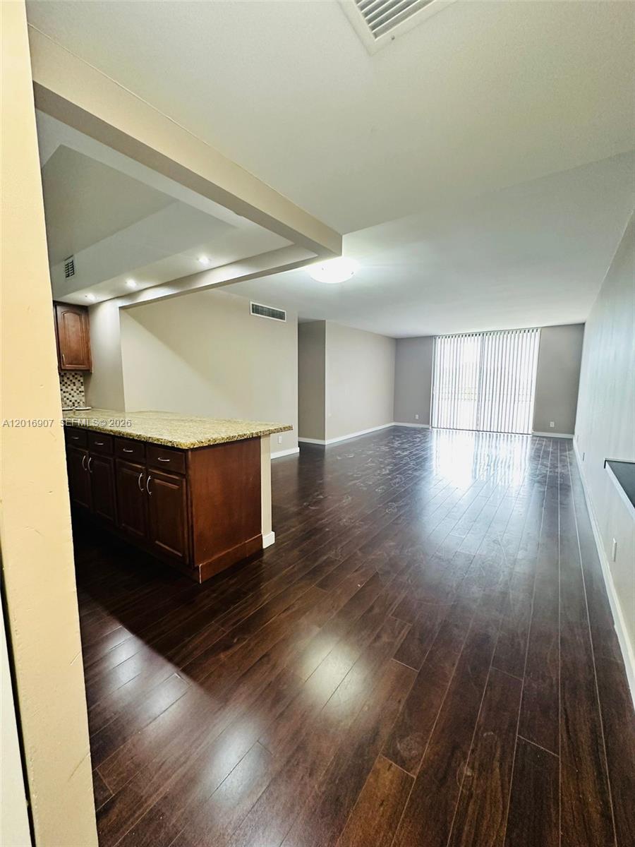 An open-concept living area features dark wood flooring, a kitchen island, and sliding glass doors — 600 Three Islands Blvd # 304, Hallandale Beach FL 33009, HALLANDALE BEACH, FL