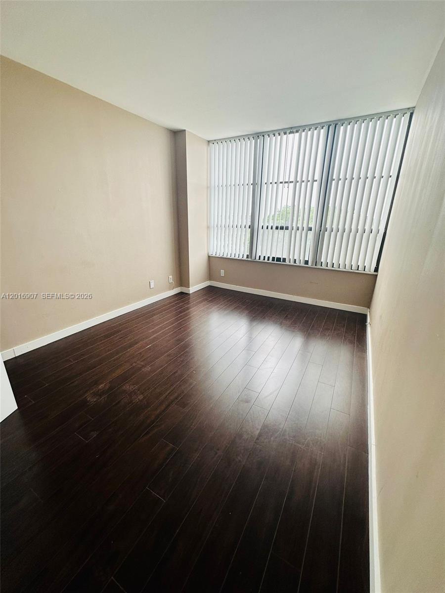 An empty room features dark wood flooring, beige walls, and large windows with vertical blinds — 600 Three Islands Blvd # 304, Hallandale Beach FL 33009, HALLANDALE BEACH, FL