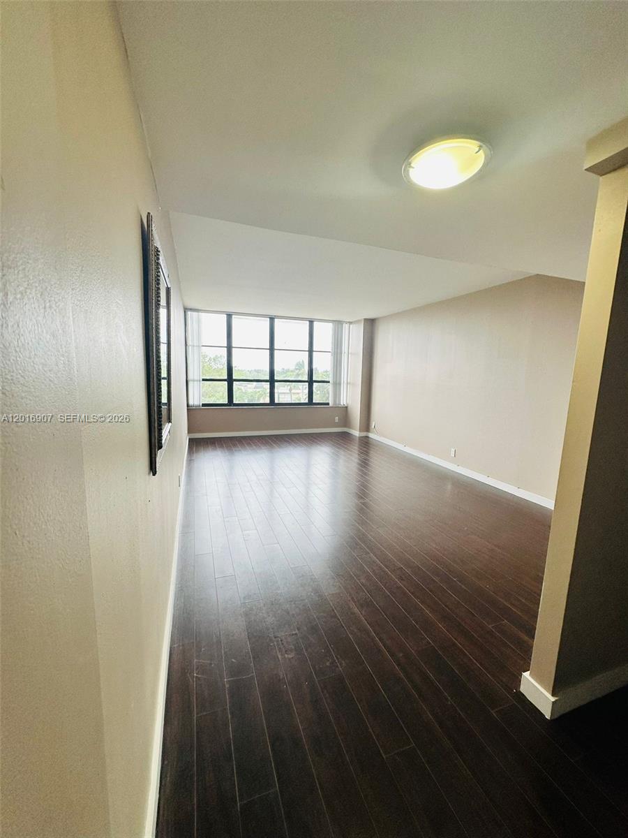 An empty room features dark wood flooring, beige walls, and a large window — 600 Three Islands Blvd # 304, Hallandale Beach FL 33009, HALLANDALE BEACH, FL
