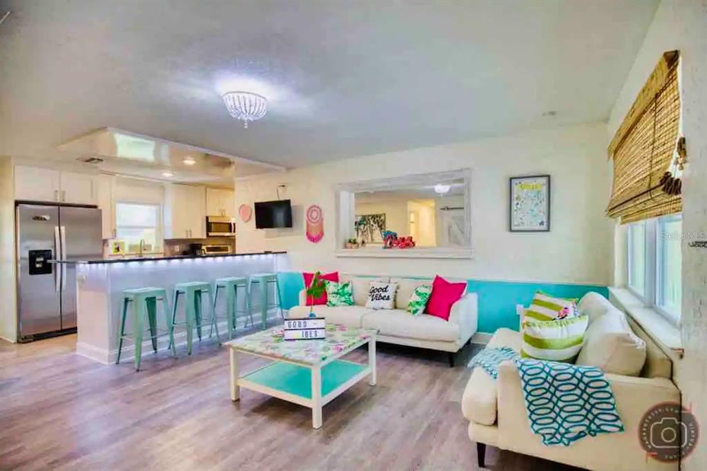 An open-concept living room and kitchen featuring a breakfast bar, white sofas, and colorful decor — 4929 BROOKMEADE DRIVE, SARASOTA, FL