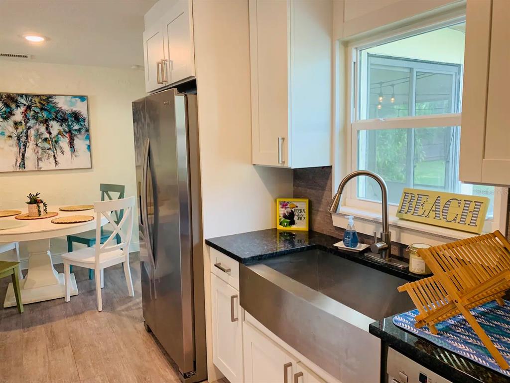 A kitchen features a stainless steel farmhouse sink, dark countertops, white cabinets, and a dining area — 4929 BROOKMEADE DRIVE, SARASOTA, FL