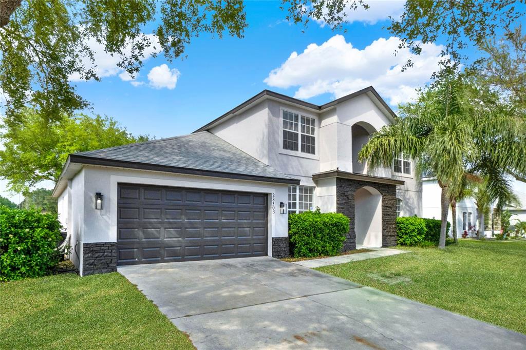 A two-story house with a gray garage, stone accents, and a palm tree in front — 23503 VALDERAMA LANE, SORRENTO, FL