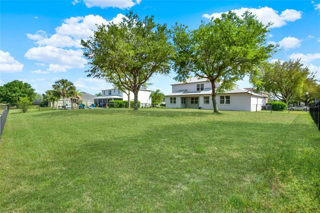 A large, grassy backyard features two mature trees and a two-story house with a fence — 23503 VALDERAMA LANE, SORRENTO, FL