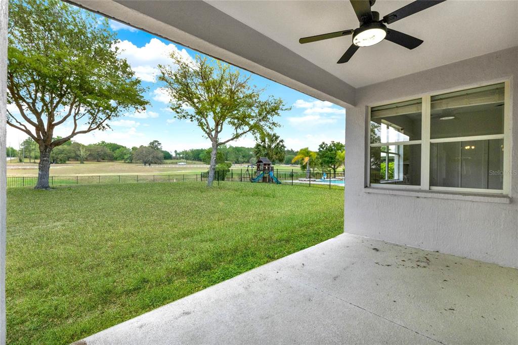 A covered concrete patio overlooks a fenced backyard with a pool and distant trees — 23503 VALDERAMA LANE, SORRENTO, FL