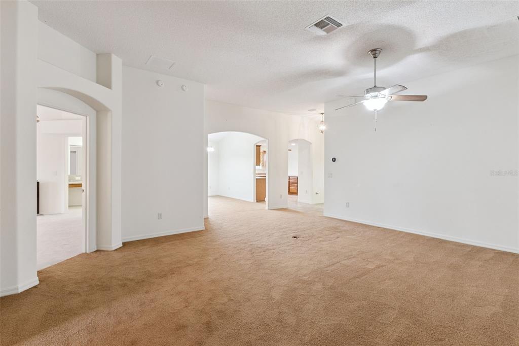 A spacious living room features beige carpeting, white walls, and a ceiling fan — 2039 TYNTE TERRACE, THE VILLAGES, FL