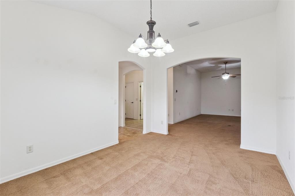 A dining area with a chandelier leads into a carpeted living space through arched openings — 2039 TYNTE TERRACE, THE VILLAGES, FL