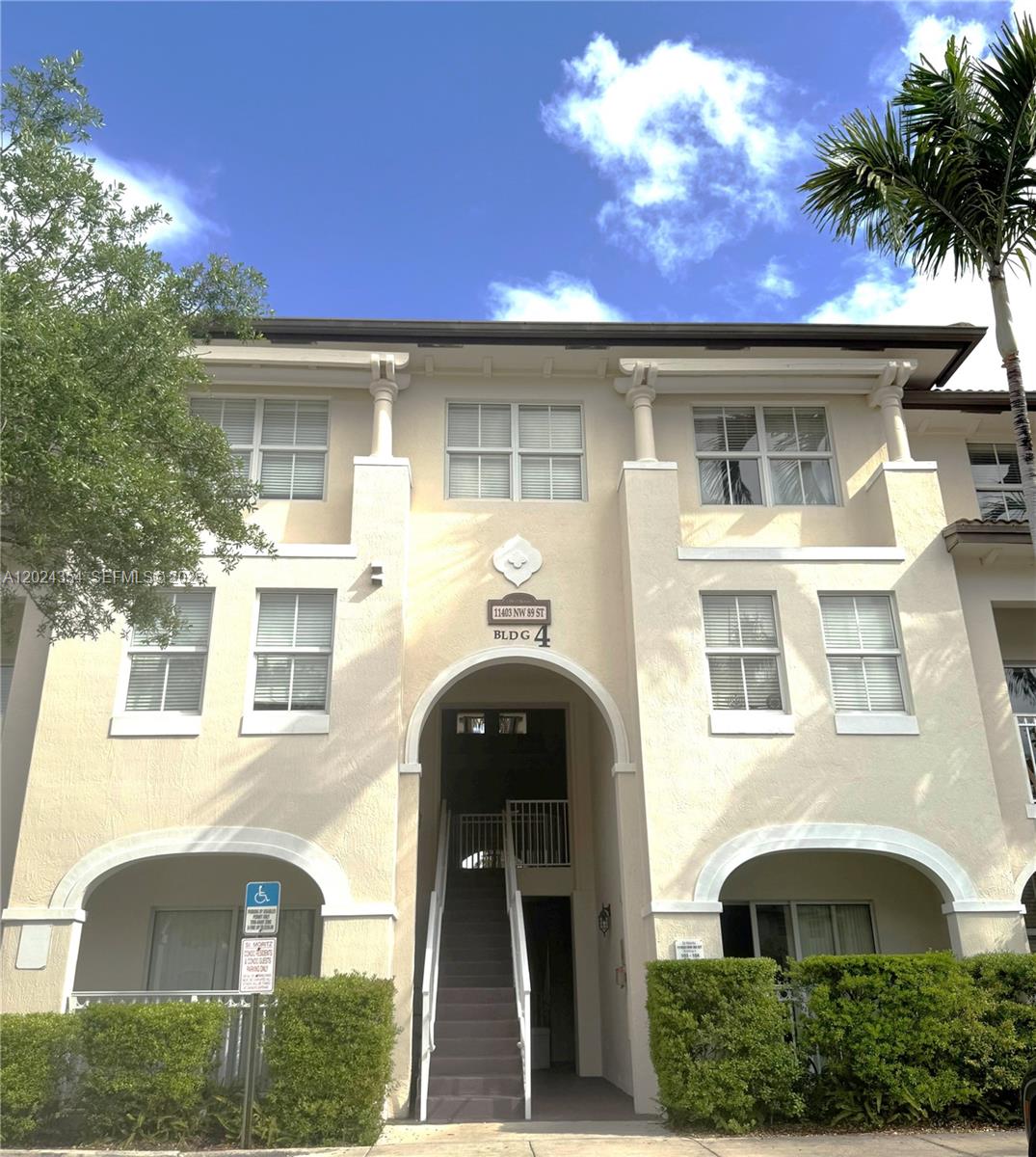 A three-story beige stucco apartment building features an arched entryway and a central staircase — 11403 NW 89th St # 208, Doral FL 33178, DORAL, FL