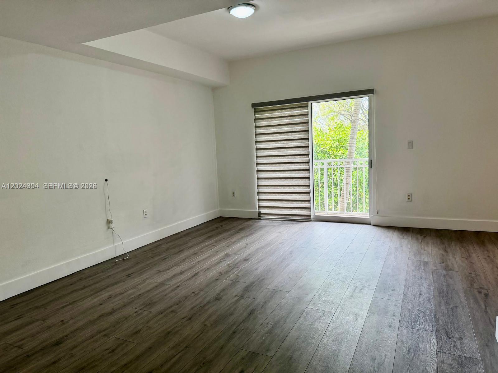 An empty room features wood-look flooring, white walls, and a sliding glass door to a balcony — 11403 NW 89th St # 208, Doral FL 33178, DORAL, FL