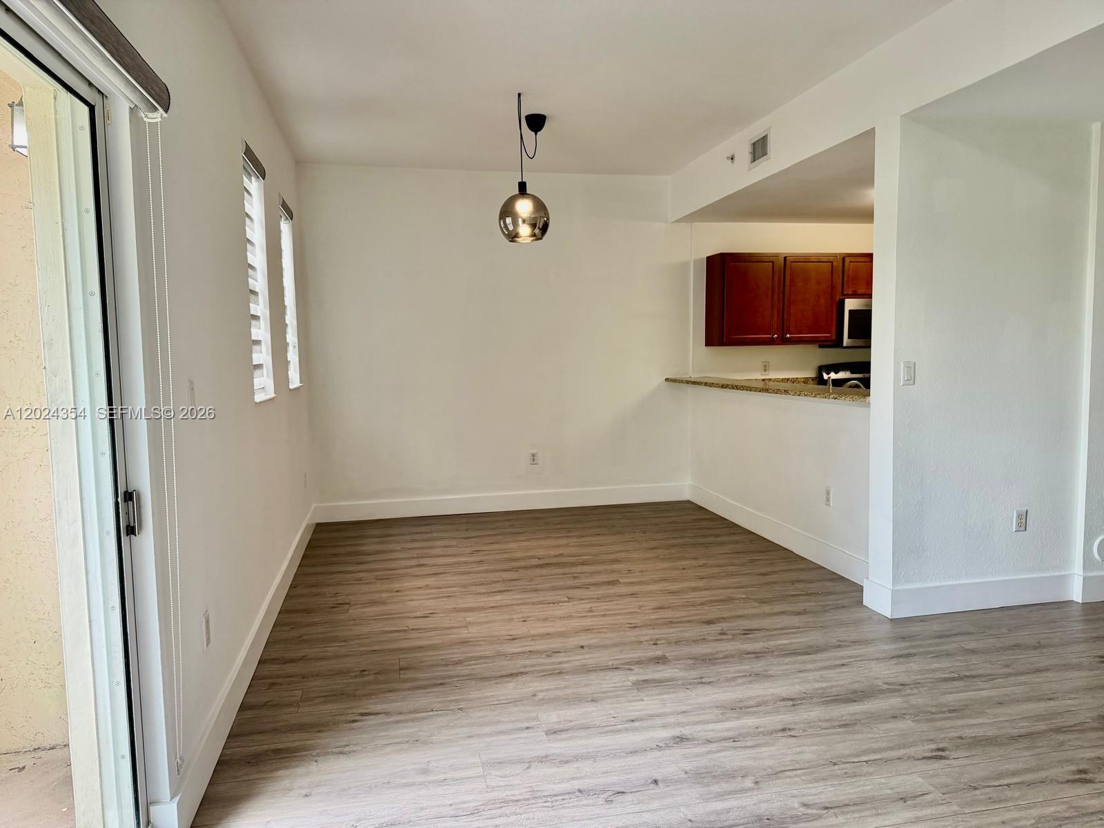 An empty dining area features wood-look flooring, a pendant light, and an adjacent kitchen counter — 11403 NW 89th St # 208, Doral FL 33178, DORAL, FL