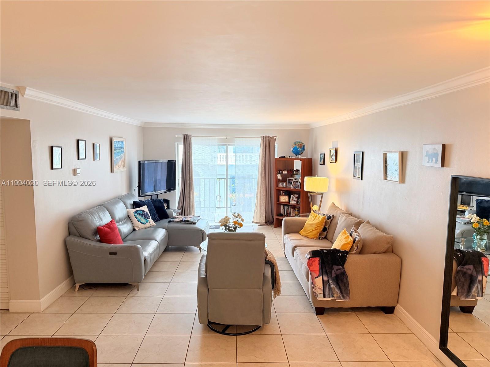 An empty room features light-colored tile flooring, neutral walls, crown molding, and a sliding glass door — 8101 SW 72nd Ave # 403W, Miami FL 33143, MIAMI, FL