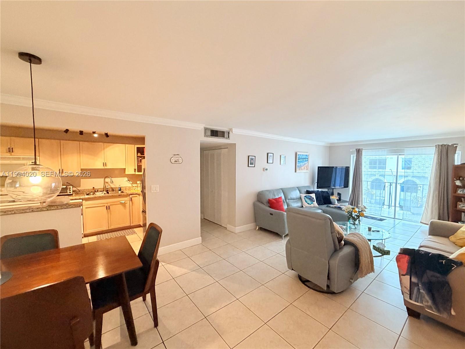 An empty living room features beige tile flooring, white walls, and a sliding glass balcony door — 8101 SW 72nd Ave # 403W, Miami FL 33143, MIAMI, FL