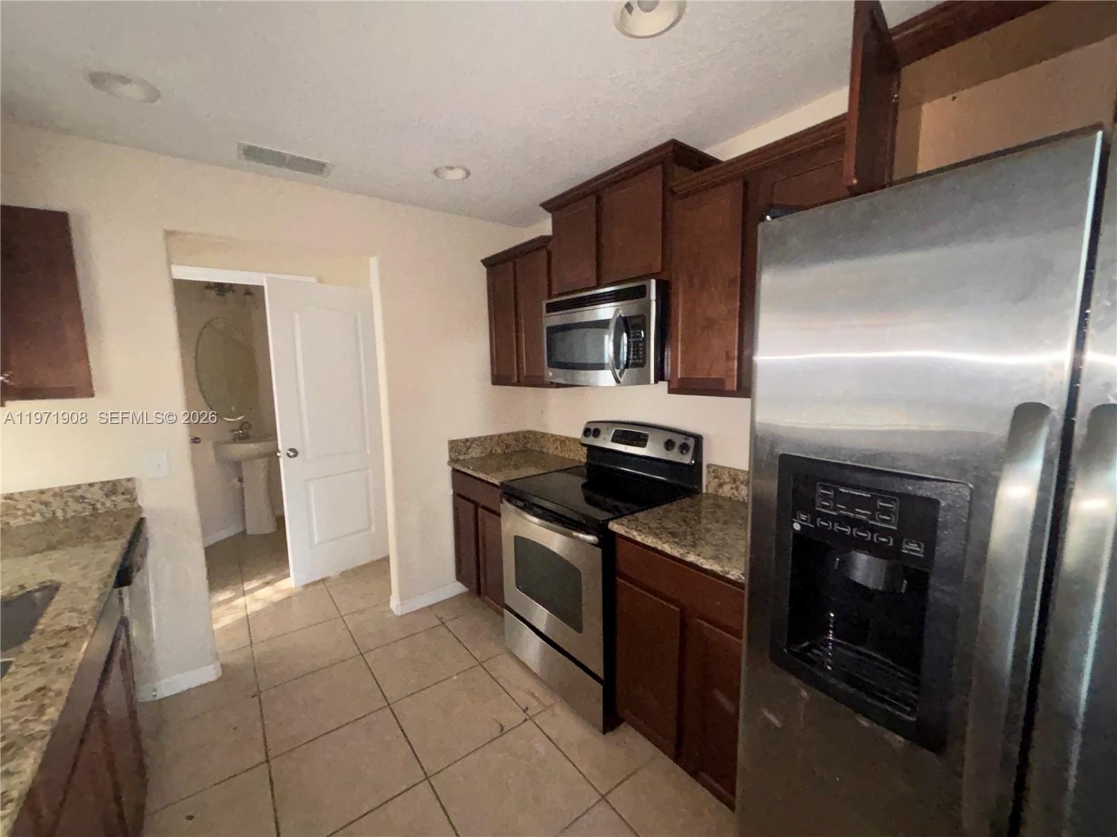 A kitchen features dark wood cabinets, stainless steel appliances, granite countertops, and tile flooring — 330 Carina Cir, Sanford FL 32773, SANFORD, FL