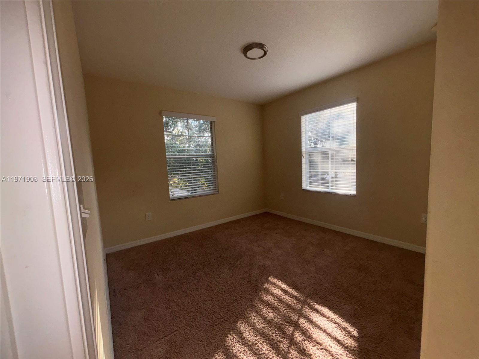 An empty bedroom features beige walls, brown carpeting, and two windows with white blinds — 330 Carina Cir, Sanford FL 32773, SANFORD, FL