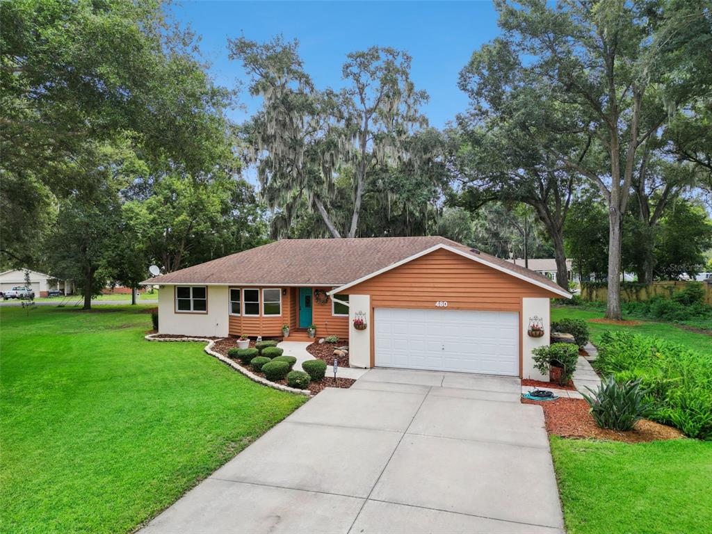A single-story house with a white and orange exterior, a two-car garage, and a concrete driveway — 480 LAKE FOREST CIRCLE, MOUNT DORA, FL