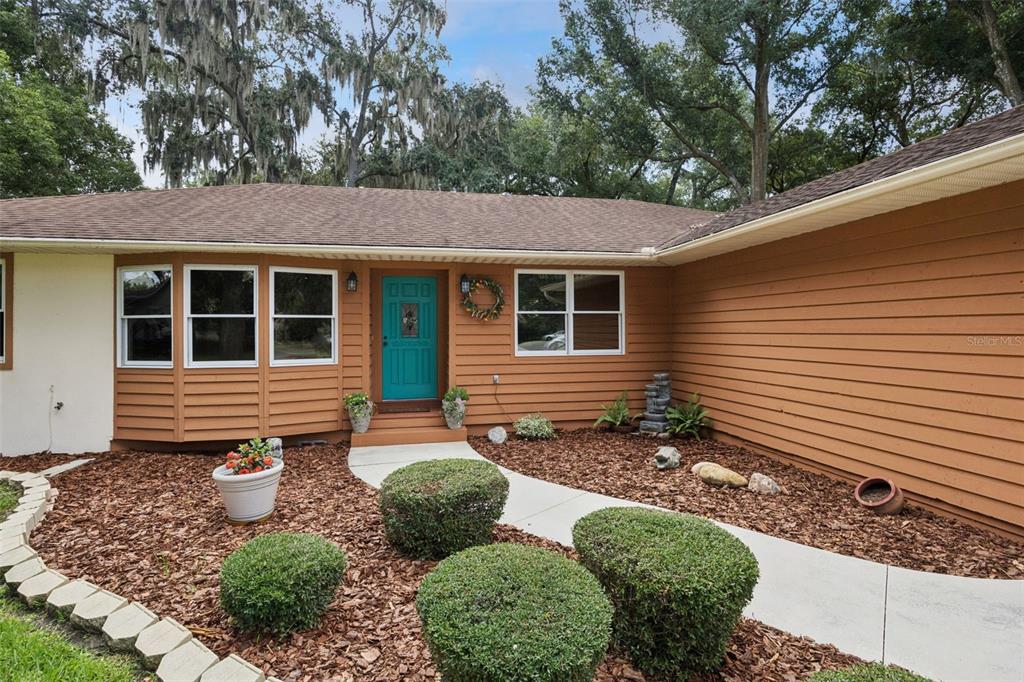 The exterior of a single-story house features brown horizontal siding, a teal front door, and landscaping — 480 LAKE FOREST CIRCLE, MOUNT DORA, FL