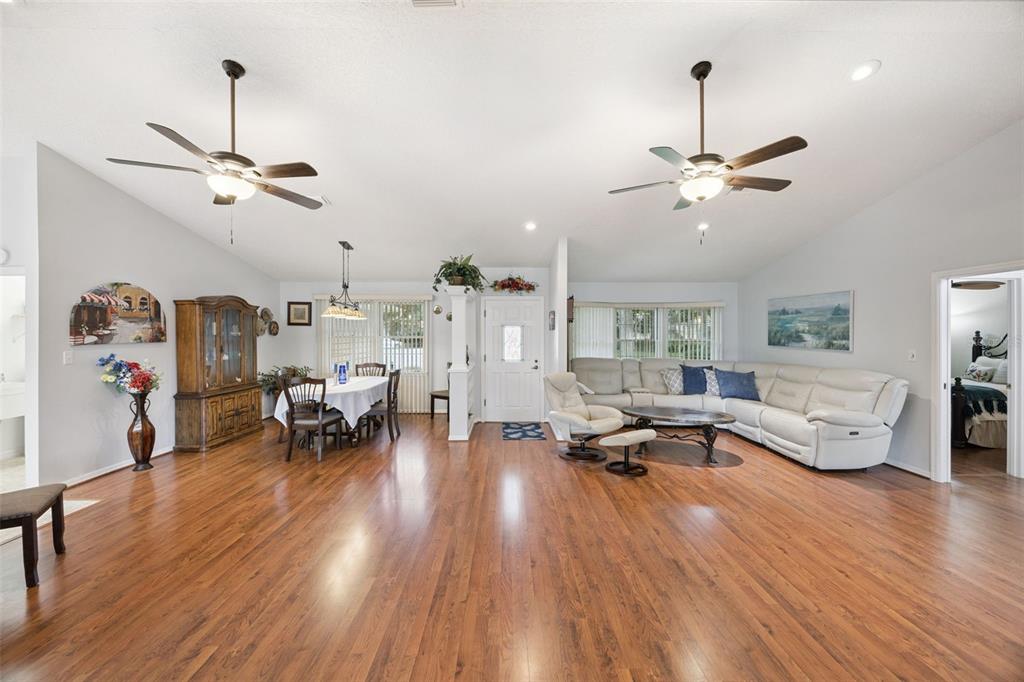 An open-concept living and dining area features hardwood floors, two ceiling fans, and white walls — 480 LAKE FOREST CIRCLE, MOUNT DORA, FL