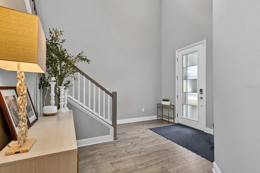 A bright entryway features light wood flooring, a staircase with white railings, and a front door — 7241 NOTCHED PINE BEND, WESLEY CHAPEL, FL