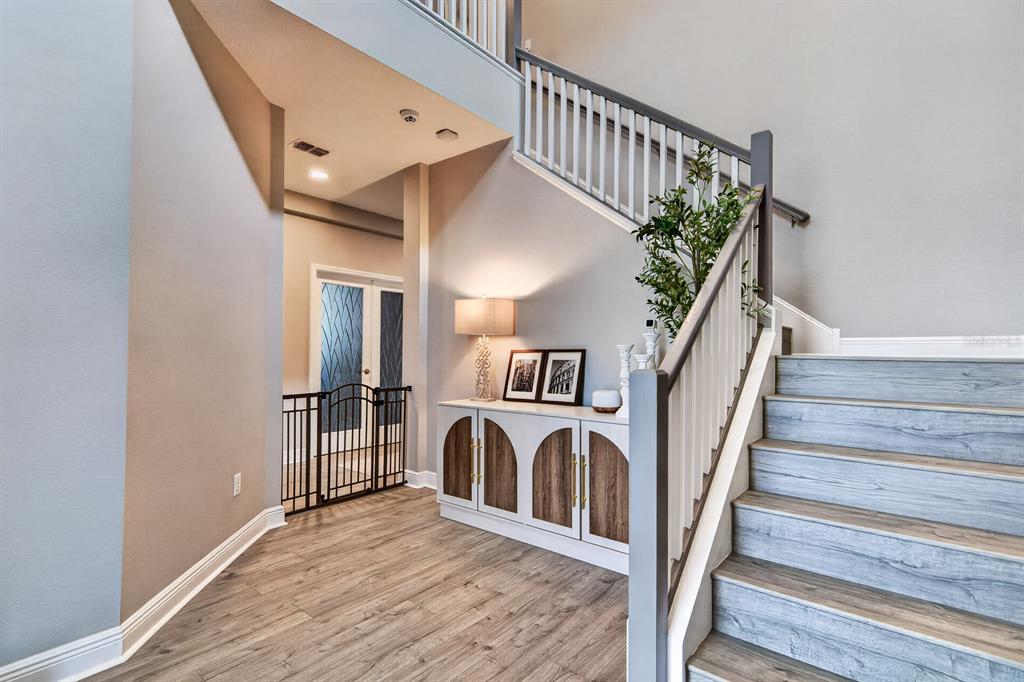 A foyer features wood-look flooring, a white cabinet, a staircase with white railings, and a gate — 7241 NOTCHED PINE BEND, WESLEY CHAPEL, FL