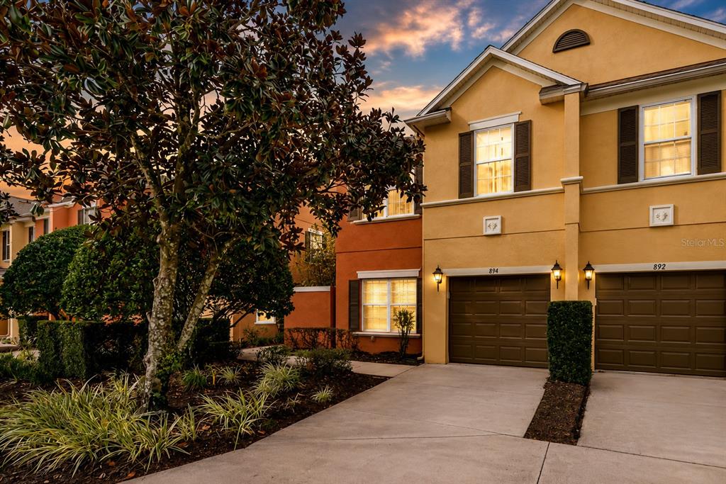 A two-story townhouse with a yellow stucco exterior and two attached garages at dusk — 894 ASSEMBLY COURT, REUNION, FL