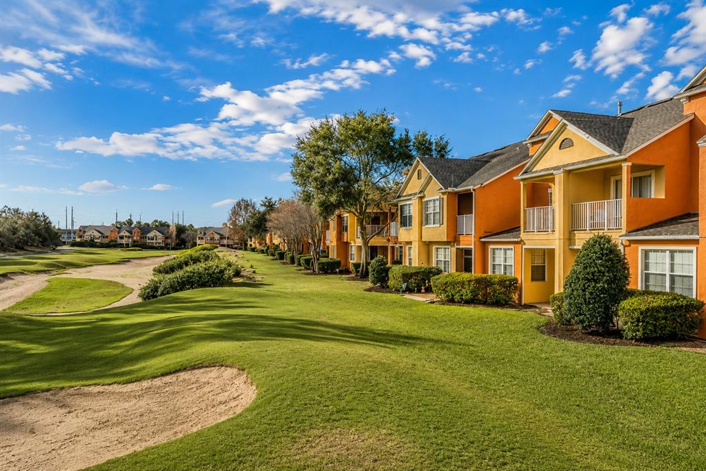 An exterior view of orange apartment buildings situated alongside a golf course fairway and bunker — 894 ASSEMBLY COURT, REUNION, FL